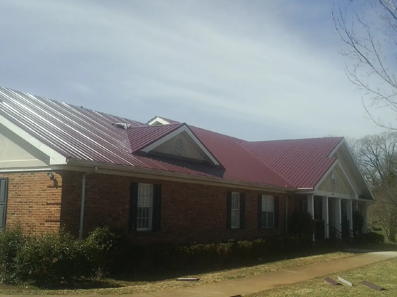 Red metal roof with gabled entries on a long brick building, from a Hail Damage Roof Repair job in Chelan Falls