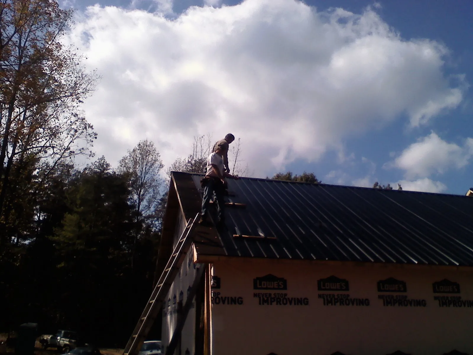Roofer fastening dark metal panels high against a cloudy sky, from a Roof Inspection job in Chelan Falls