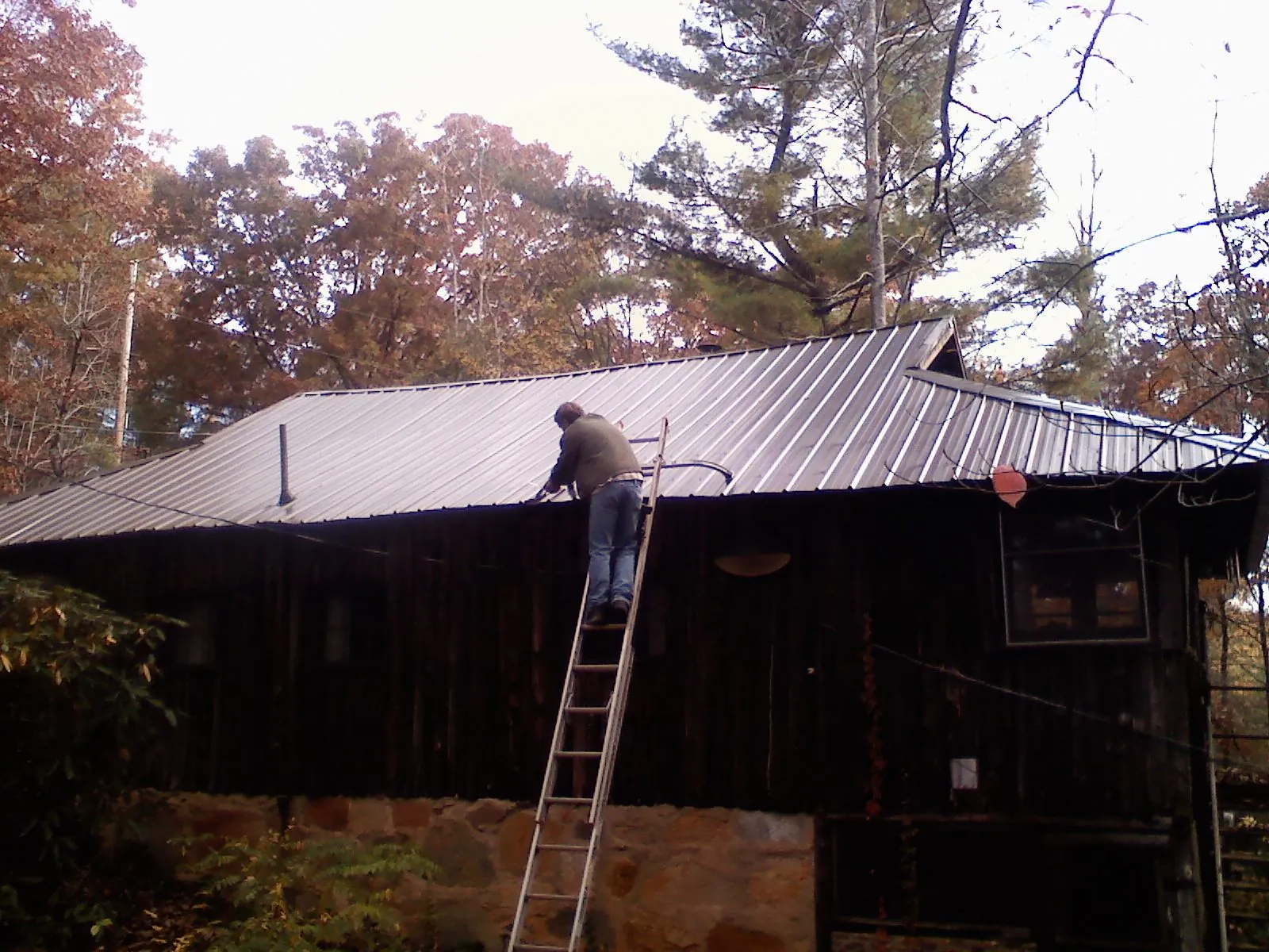 Roofer on a ladder working along the edge of a cabin metal roof in Chelan Falls