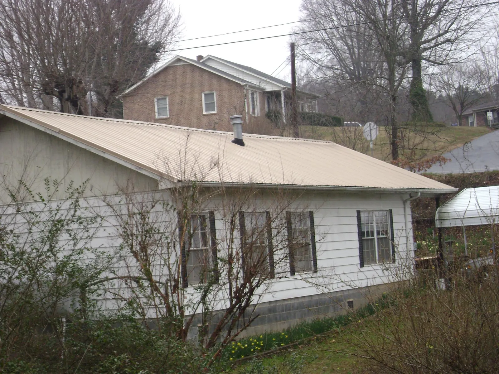 Tan metal roof on a white sided house set into a hillside — Commercial Roofing by Roofing Brothers in Chelan Falls